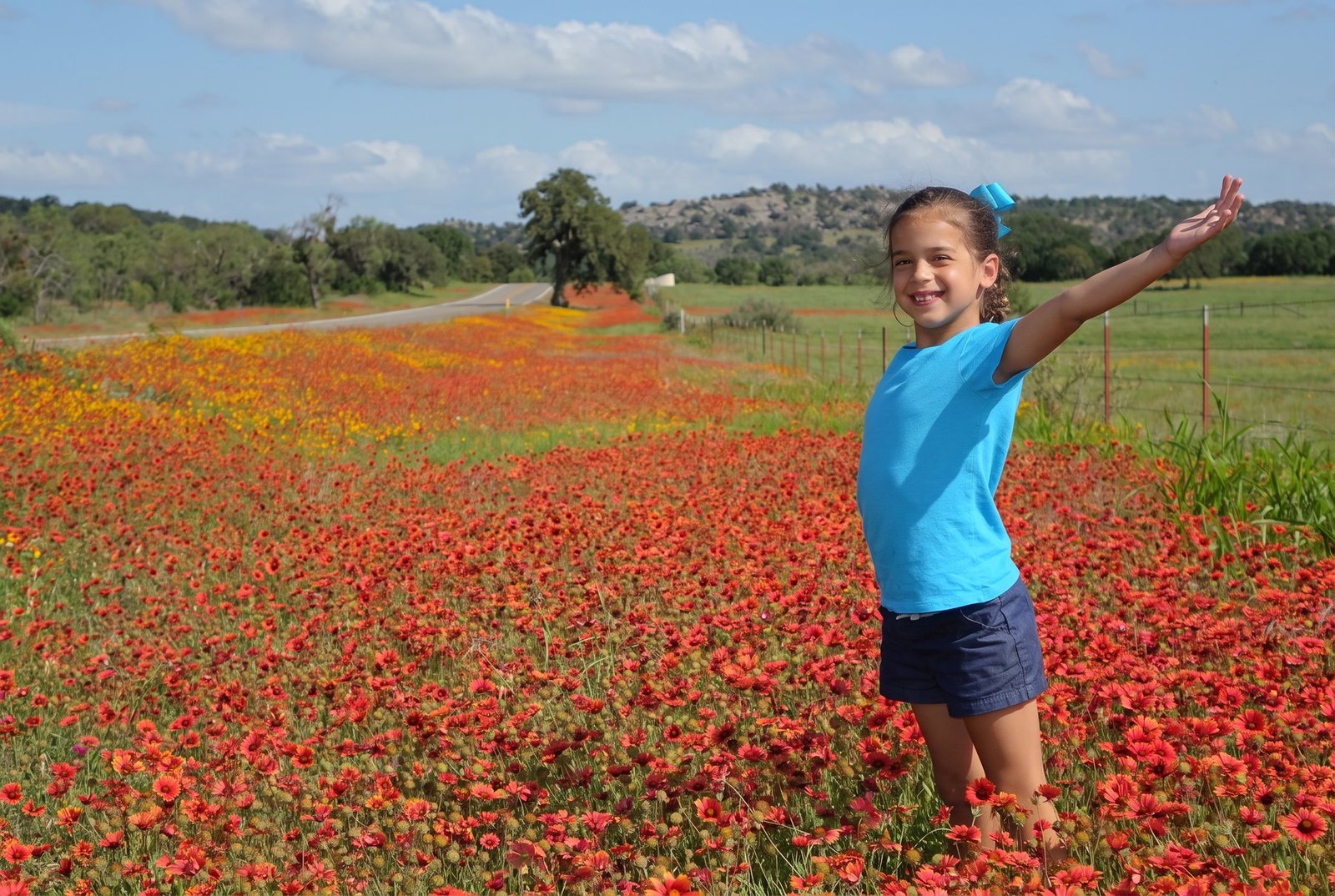 A child standing with arms outstretched in a field of Texas wildflowers