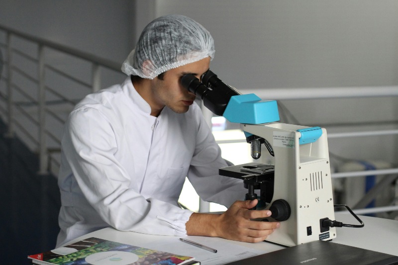 A researcher in a white lab coat focusing on a microscope